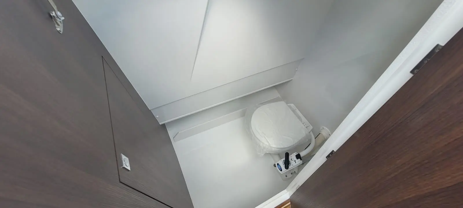 View of a modern bathroom featuring a white toilet wrapped in plastic, minimalist décor, and wooden door.